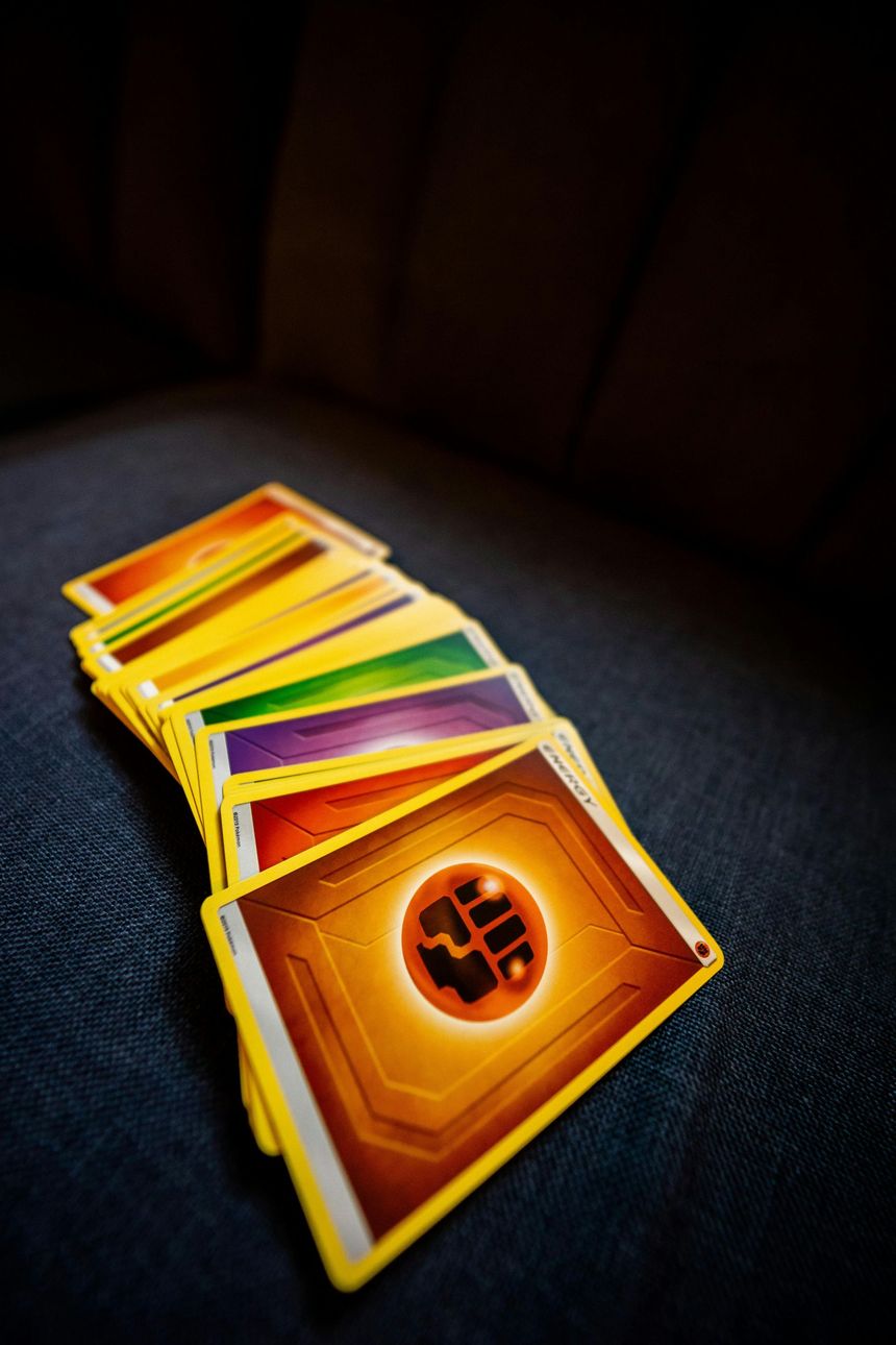 Stack of colorful trading cards on a dark fabric surface, with one orange card showing a circular emblem