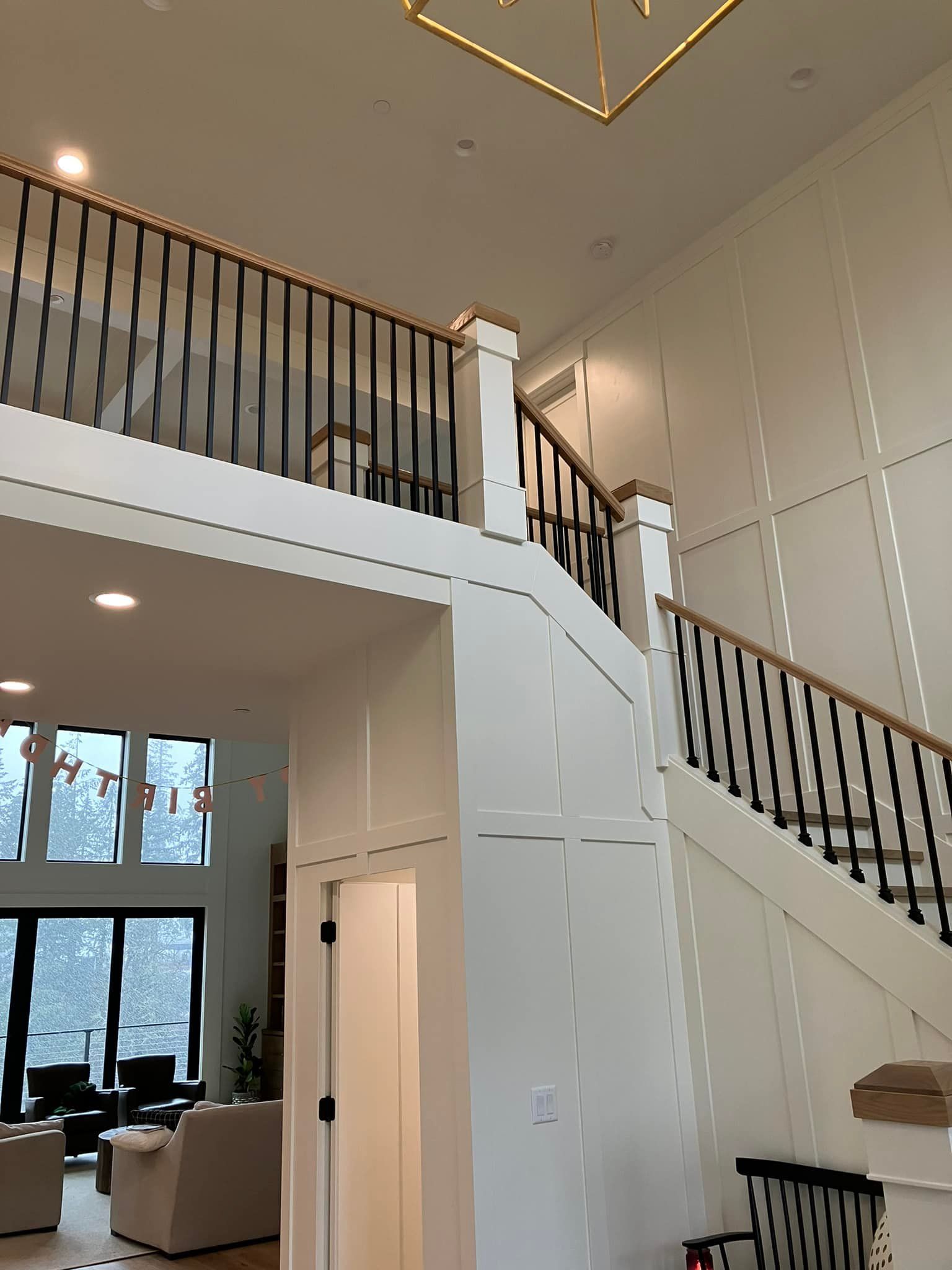 A two-story entryway with white wainscoting, black railings, and a view into a living room with floor-to-ceiling windows.