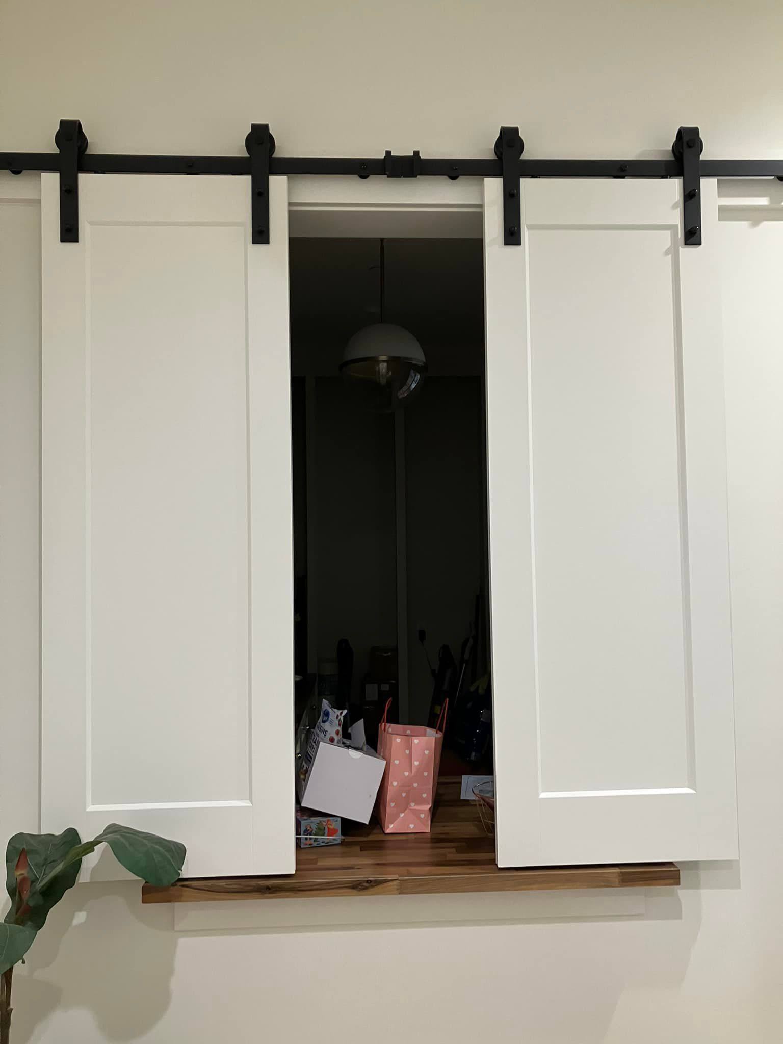 Two white shutter-style doors on a black sliding rail mounted over an indoor window opening with a wood ledge.