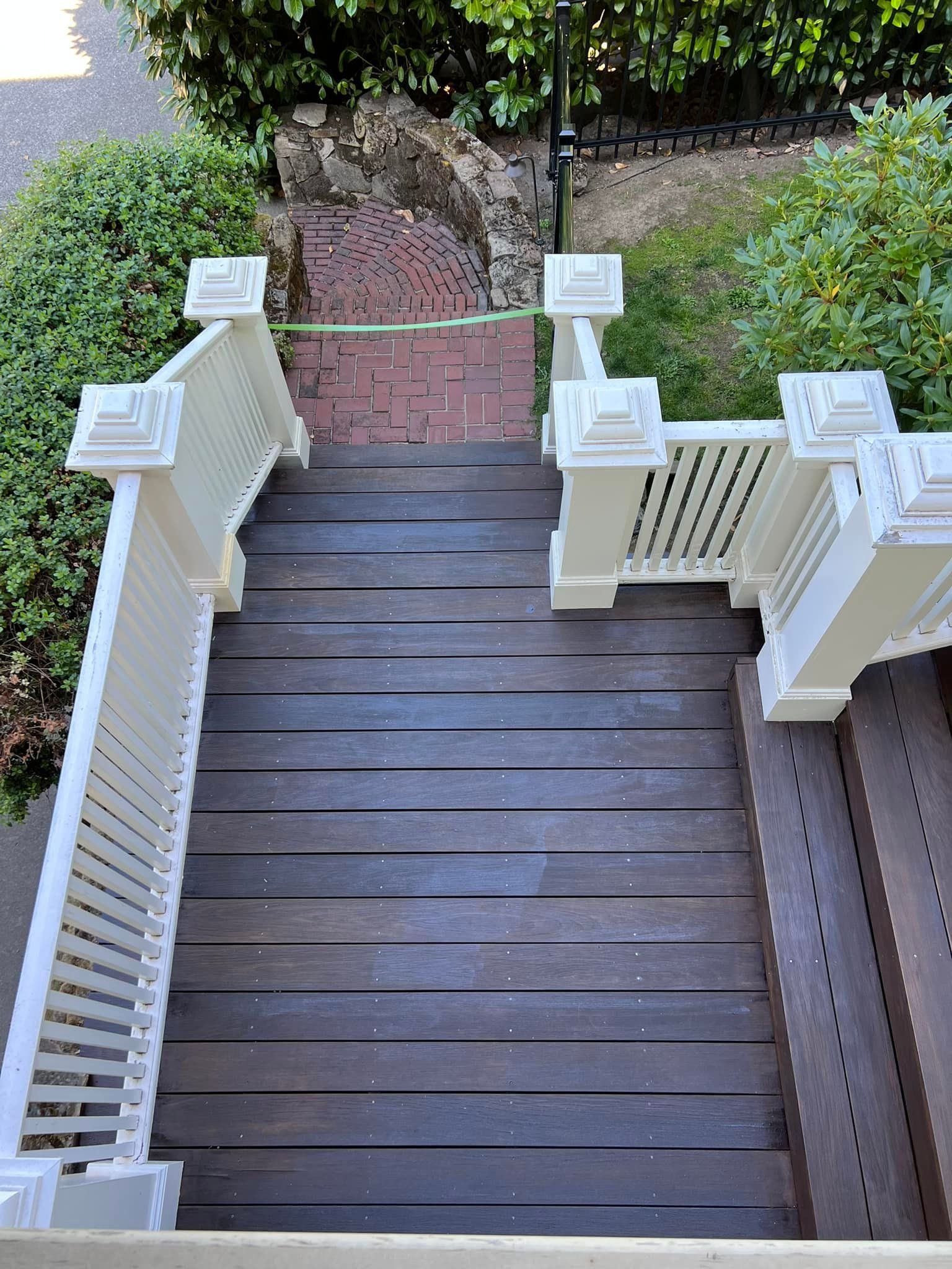 A high-angle view of outdoor wooden stairs with white railings leading down to a red brick walkway.