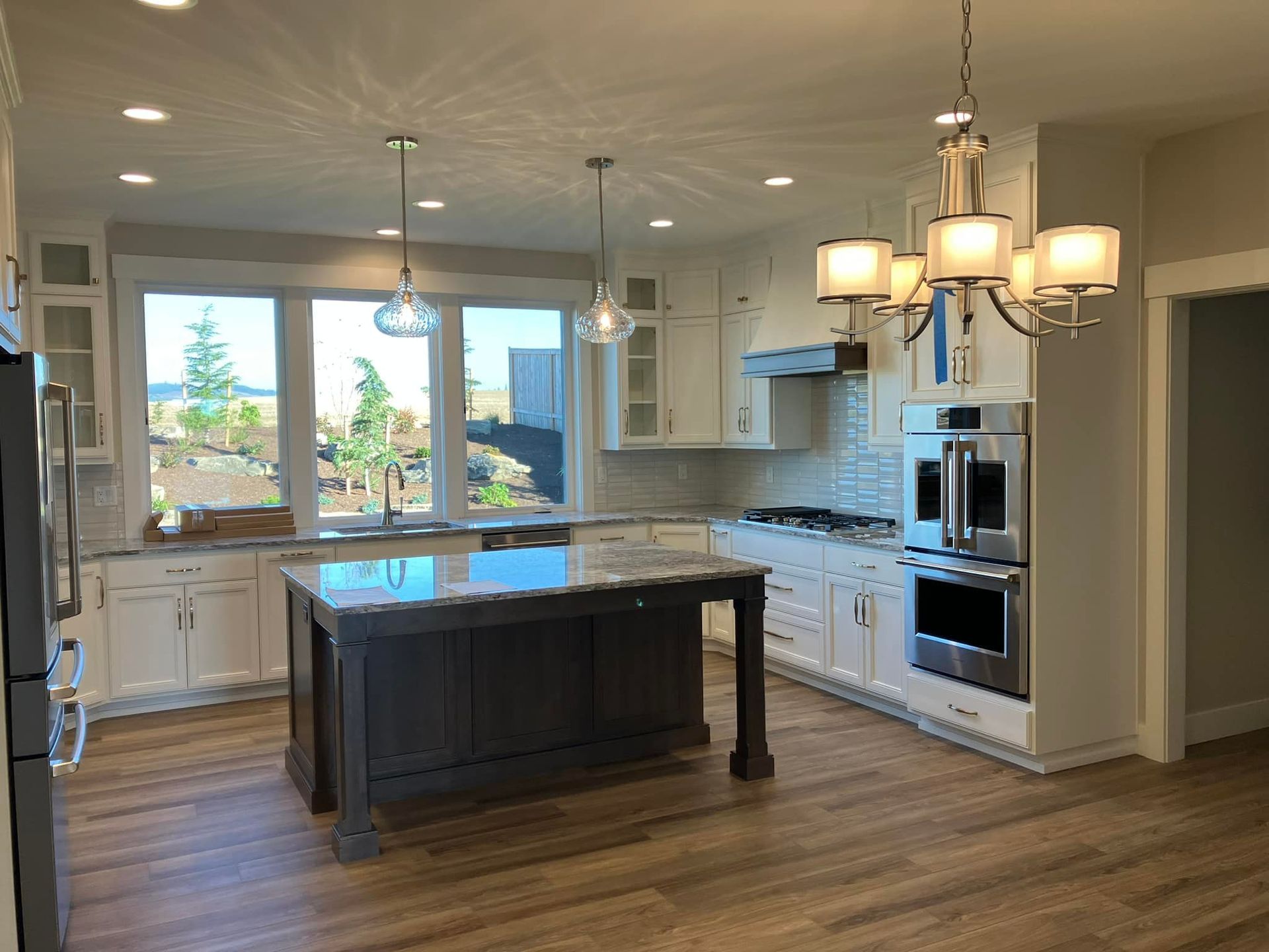 A well-lit kitchen features white cabinets, a dark wood central island with a marble top, and a chandelier over the island.