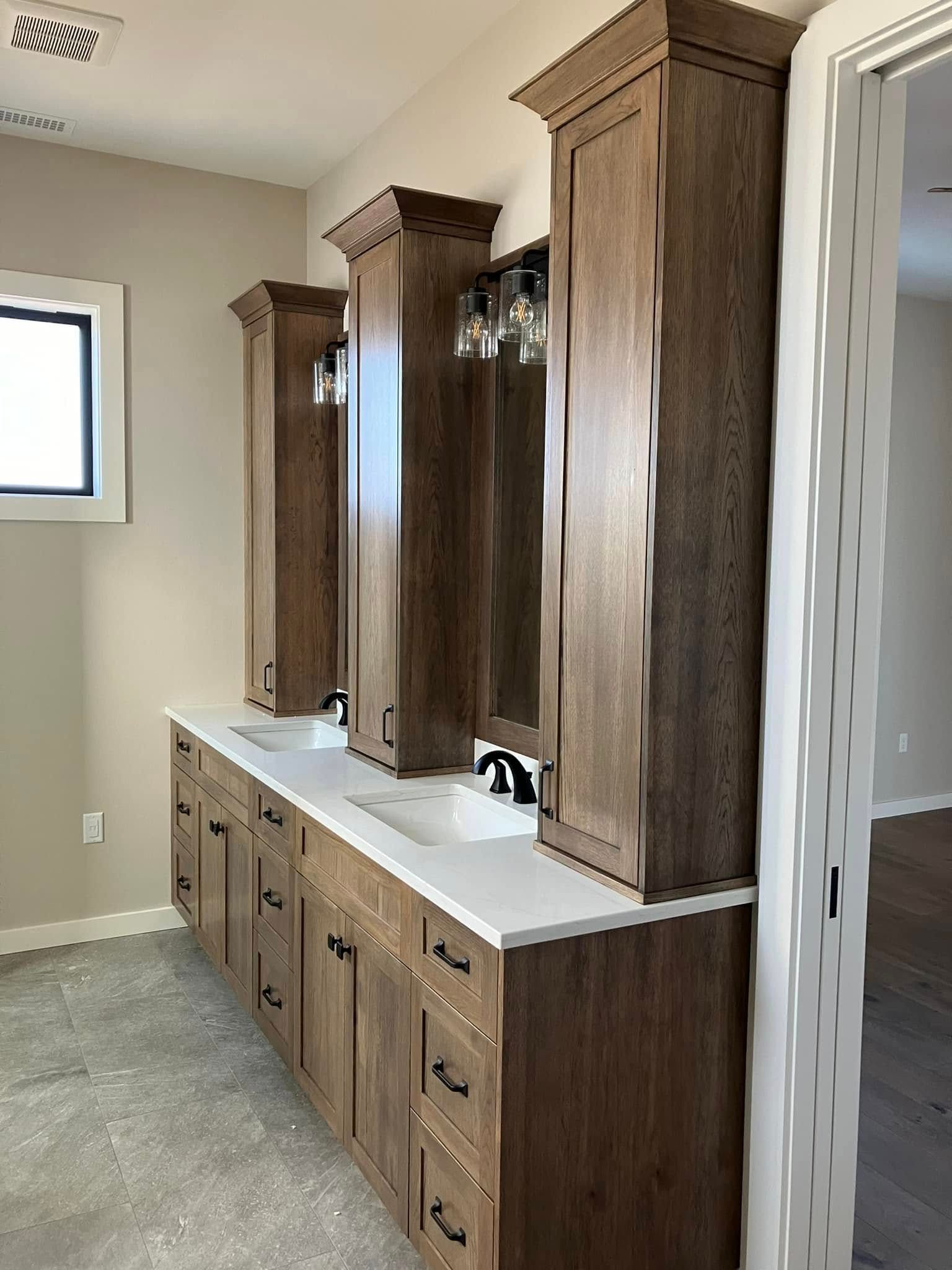 A bathroom vanity with dark wood cabinets, white countertops, two sinks, and two matching tall vertical wall cabinets.