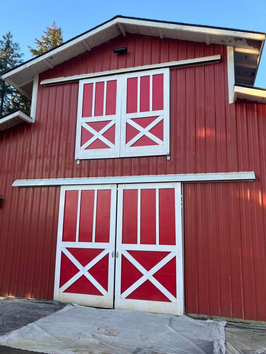 A red barn with white-trimmed sliding doors and a loft door, set against a blue sky.