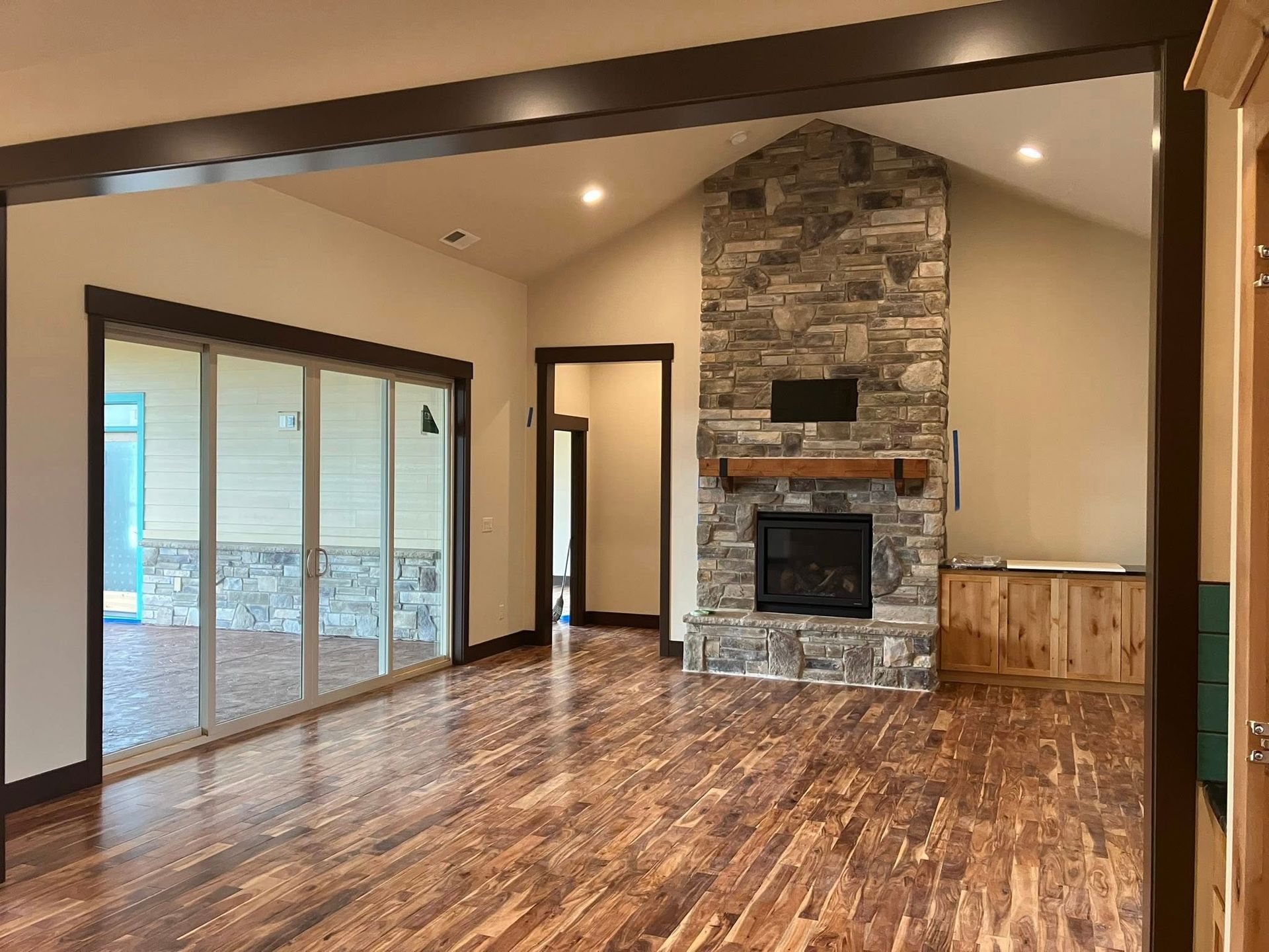 A living room with hardwood floors, a stone fireplace, built-in wooden cabinets, and large glass sliding doors.