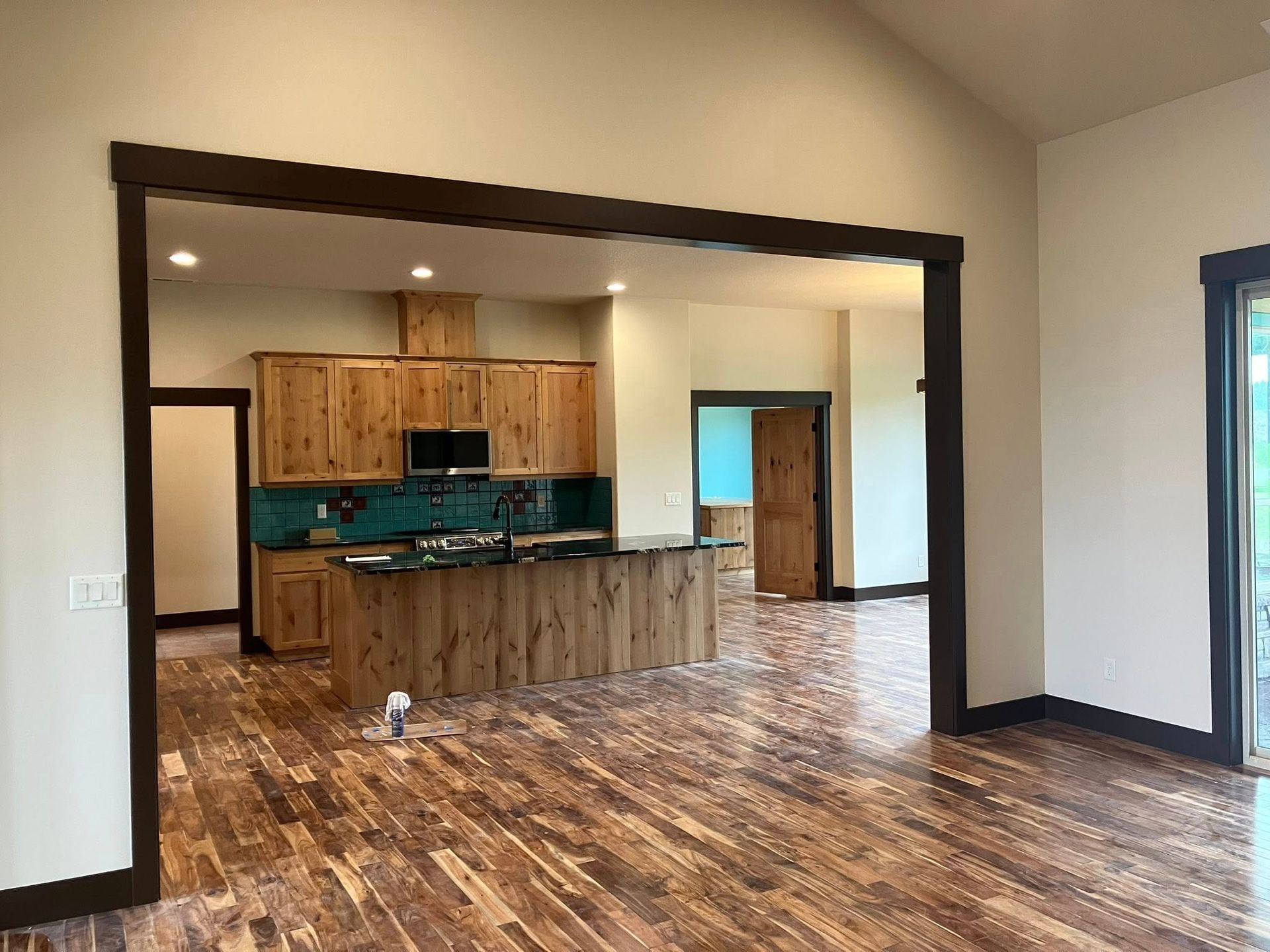 An open-concept interior view featuring rustic wood cabinets, a kitchen island, and hardwood floors framed by dark trim.