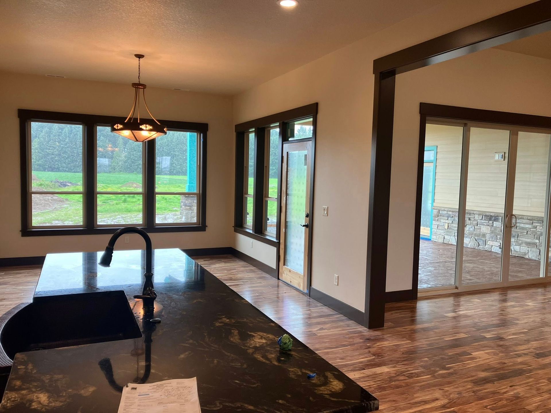 A modern kitchen featuring a dark granite island, brown wood-trimmed windows, and sliding glass doors leading to a patio.