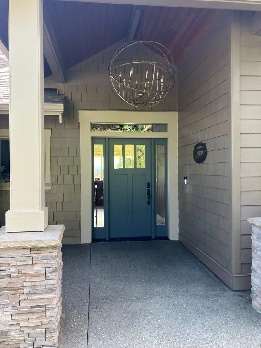 A front entrance with a blue door, a round metal chandelier hanging above, tan siding, and a stone pillar base.