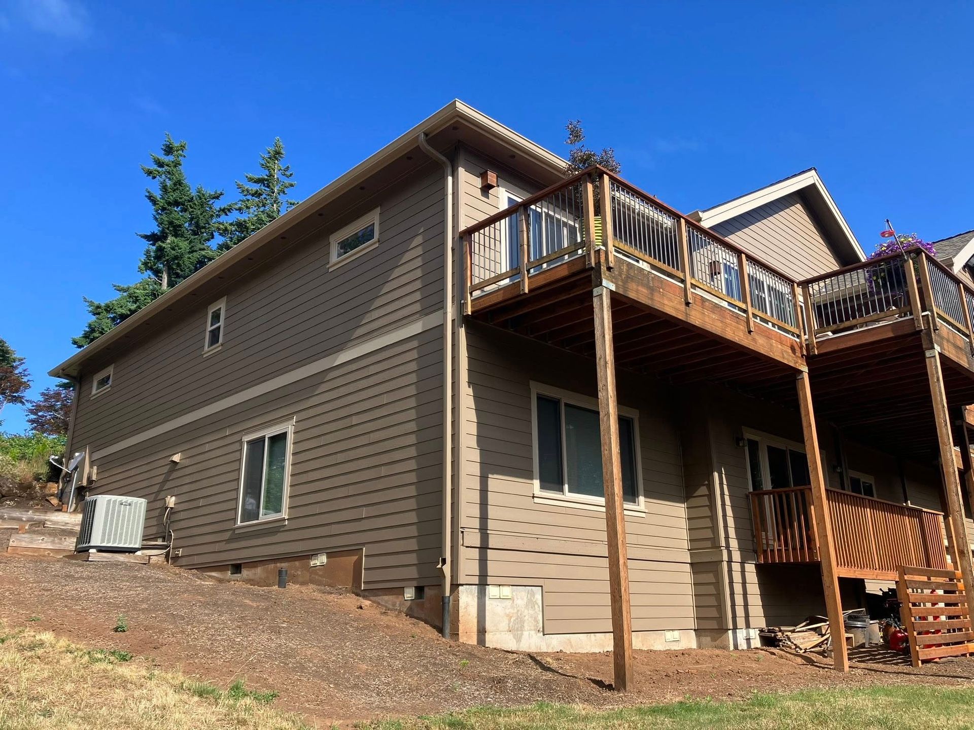 Two-story house with brown horizontal siding, a large wooden deck, and an air conditioning unit on a sloped grassy yard.