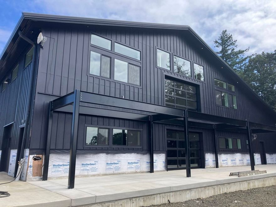 A partially finished modern, dark-sided building with black steel beams and an exposed white underlayment on the lower half.