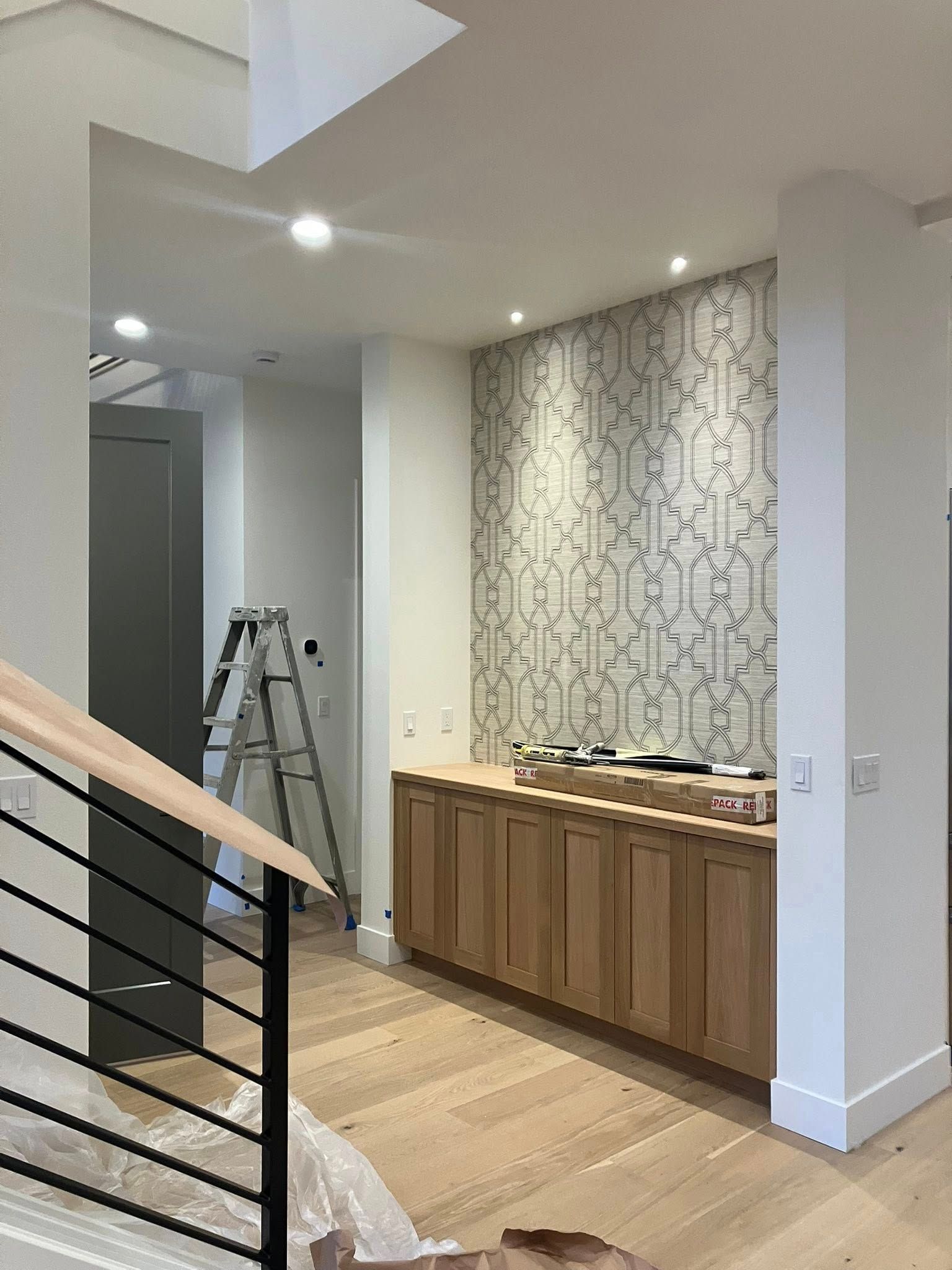 Modern home interior featuring light wood cabinets, patterned wall tile, a metal staircase railing, and a step ladder.