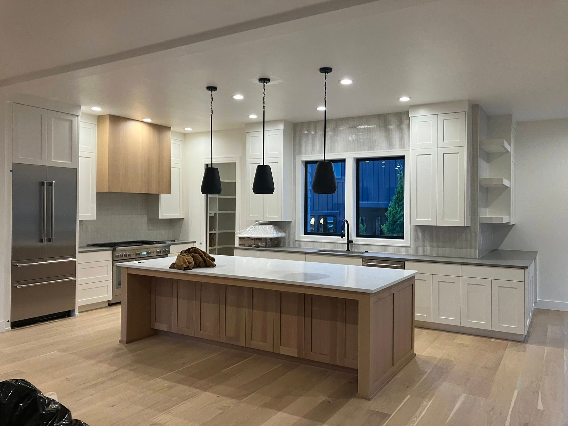 Modern kitchen with a light wood island, white cabinets, stainless steel refrigerator, and three black pendant lights.