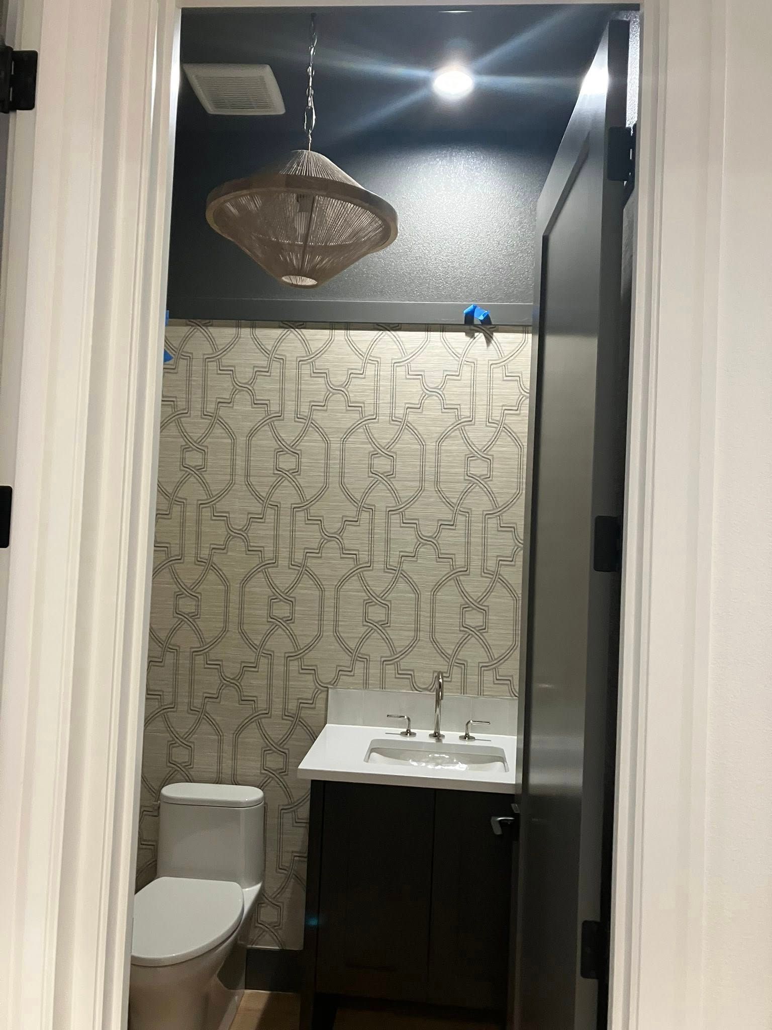A small powder room with patterned wallpaper, a dark vanity, a white toilet, and a pendant light fixture.