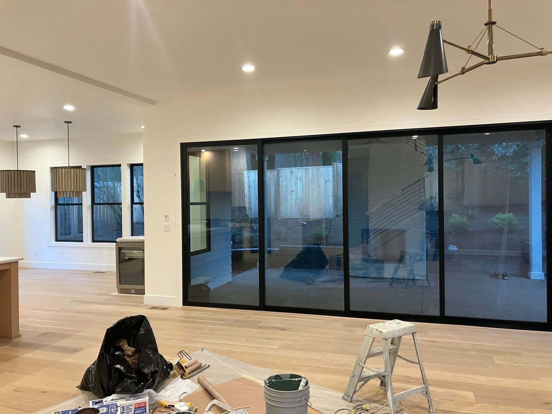 Interior of a room under construction with light wood floors, a large four-panel sliding glass door, and modern lighting.