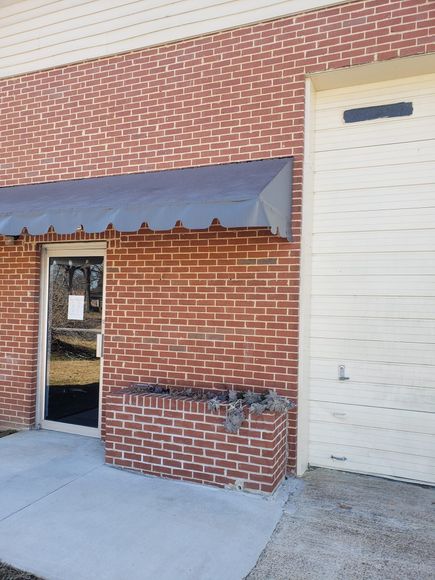 Brick building exterior with a glass door, gray awning, and a roll-up door.