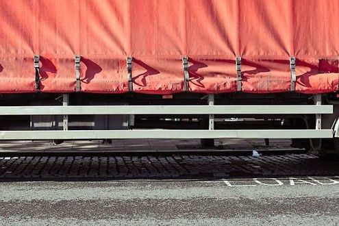 Red-covered truck side with metal rails, parked on cobblestones and asphalt.