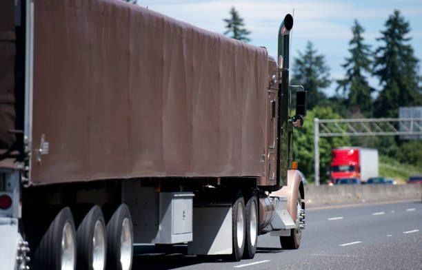 Brown semi-truck on highway; another red truck in the distance.