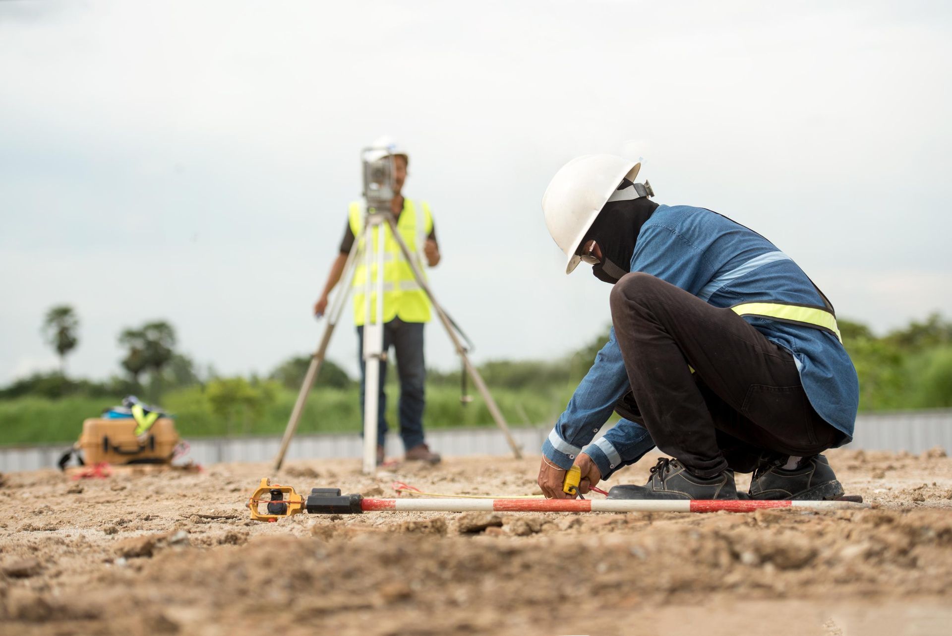 Two construction workers surveying a site with surveying equipment and measuring. 