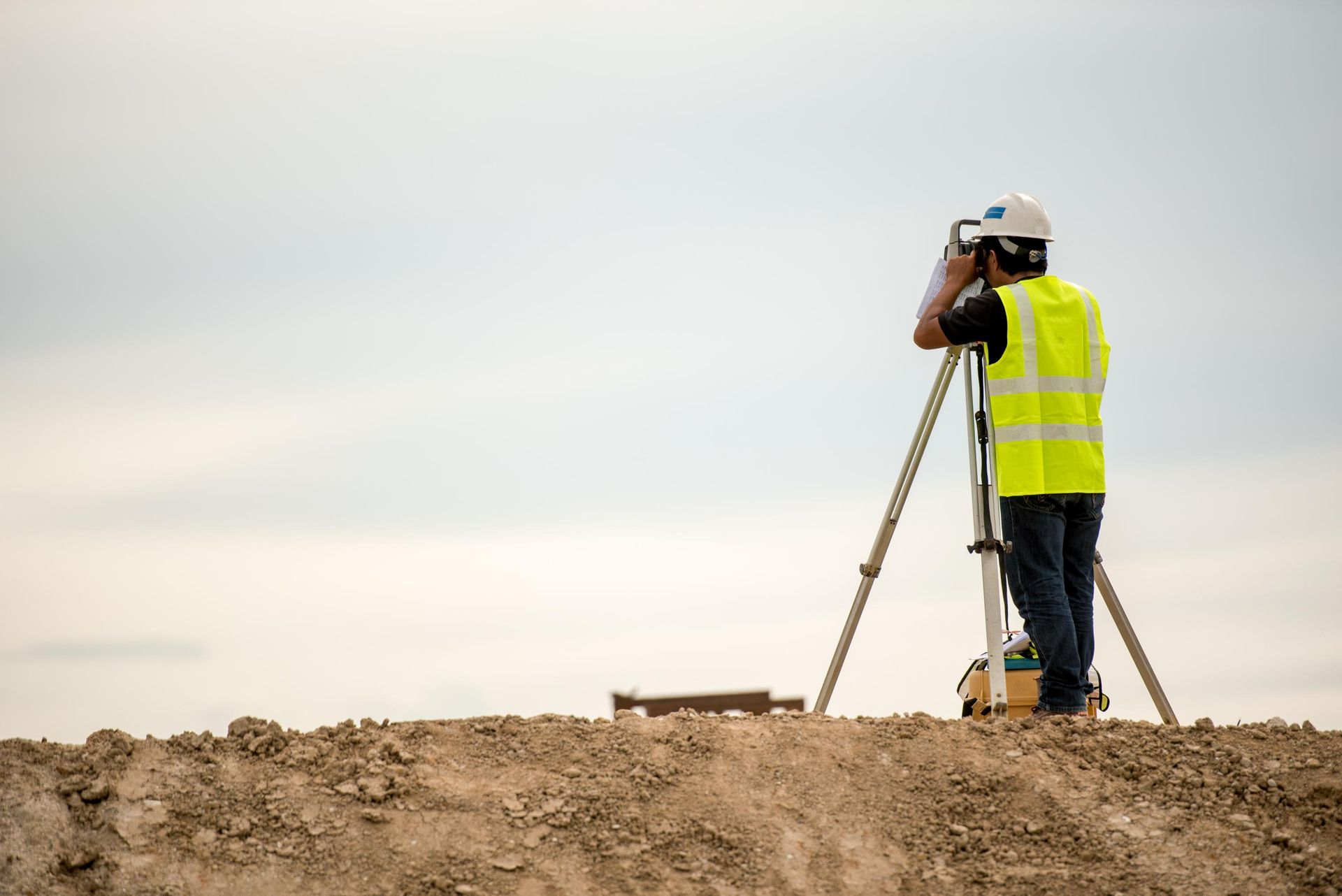 Surveyor in a reflective vest using surveying equipment outdoors.