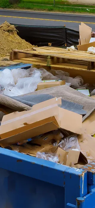 A blue dumpster filled with cardboard boxes and pallets.
