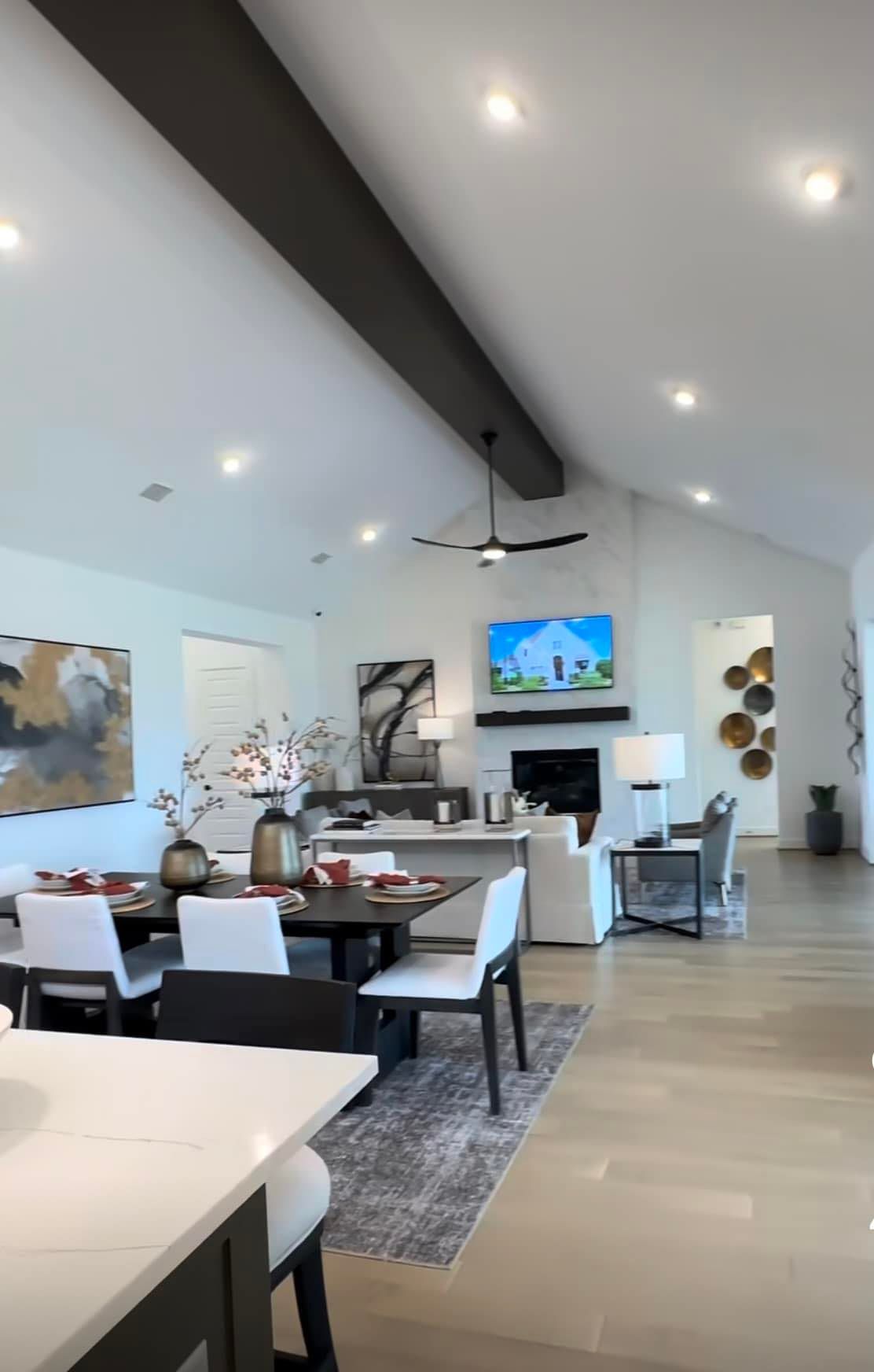 A living room with a dining table and chairs and a television on the wall.