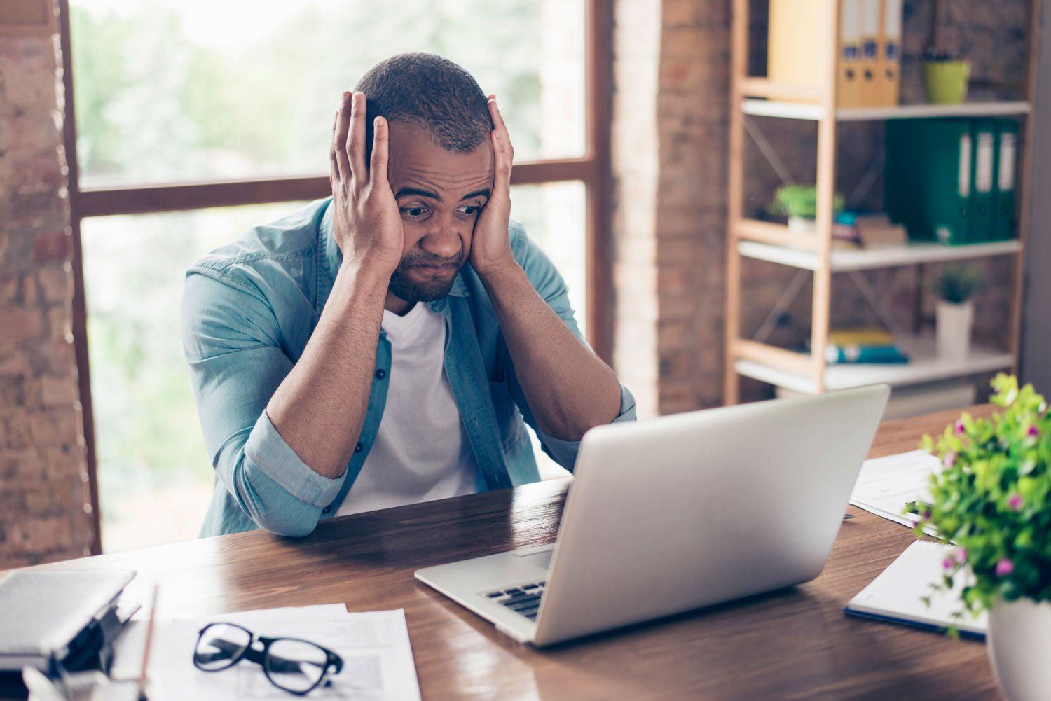 A man is sitting at a desk looking at a laptop computer.