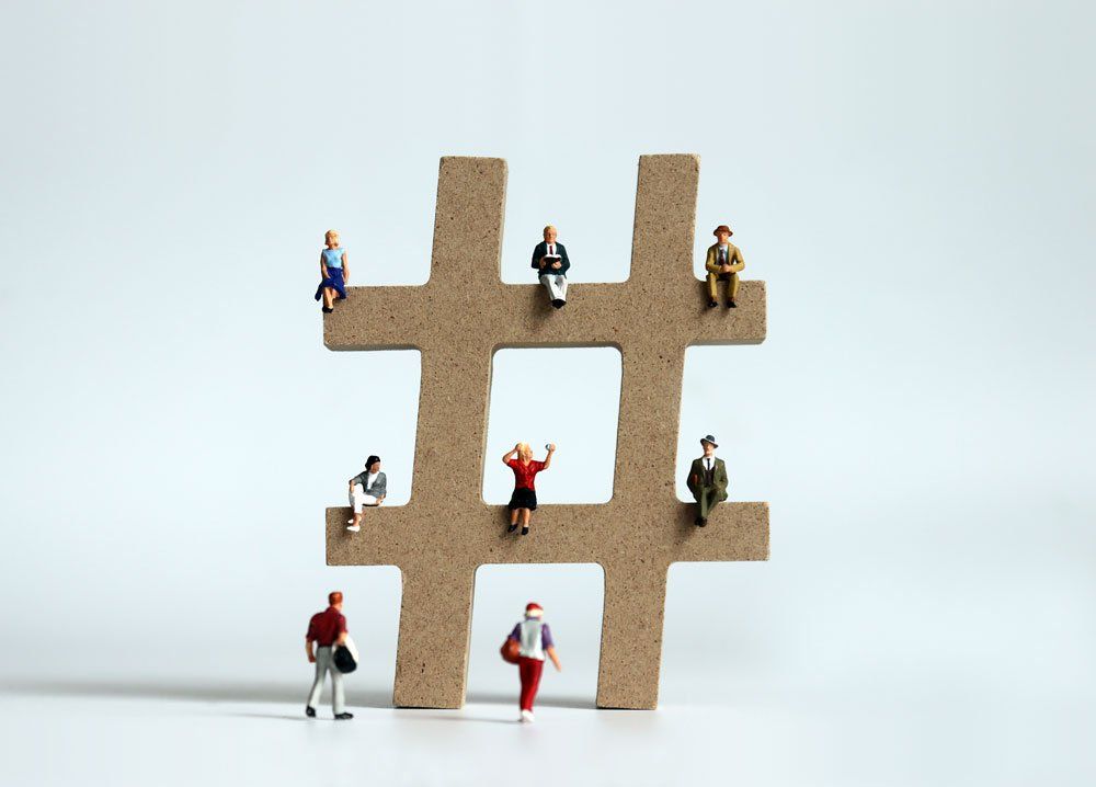 A group of miniature people are sitting on top of a wooden hashtag sign.