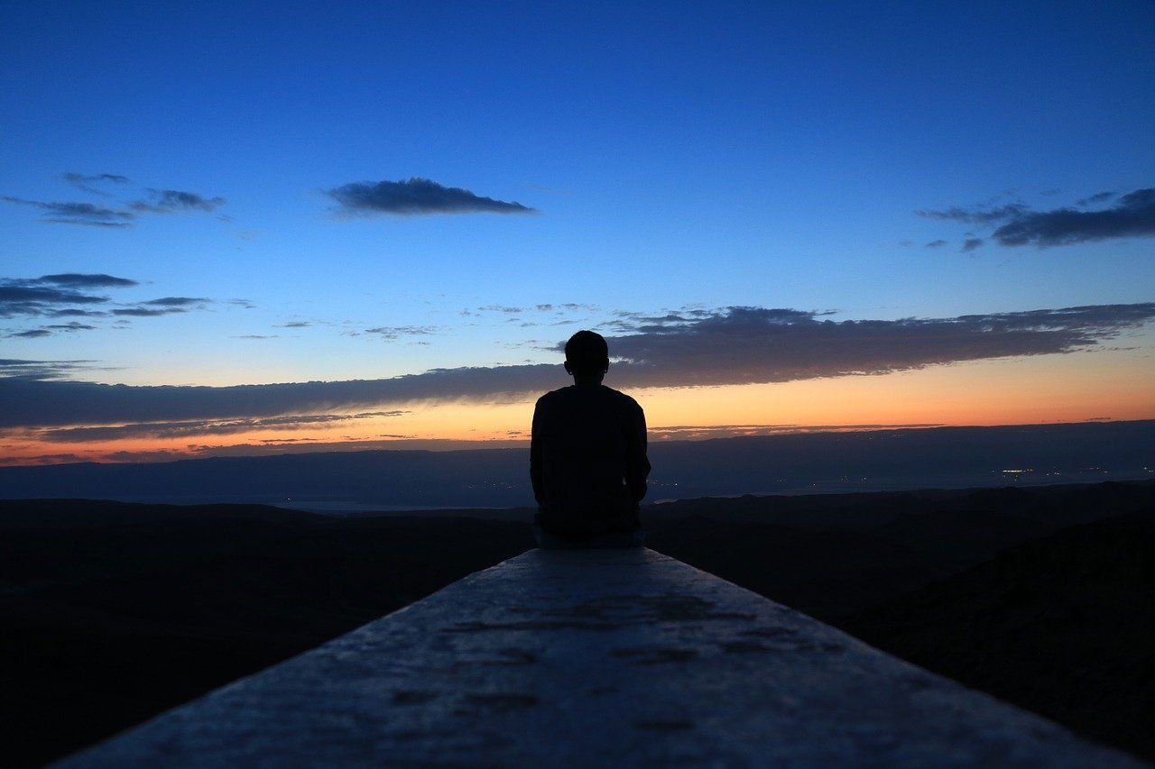 A silhouette of a person standing on top of a hill at sunset.