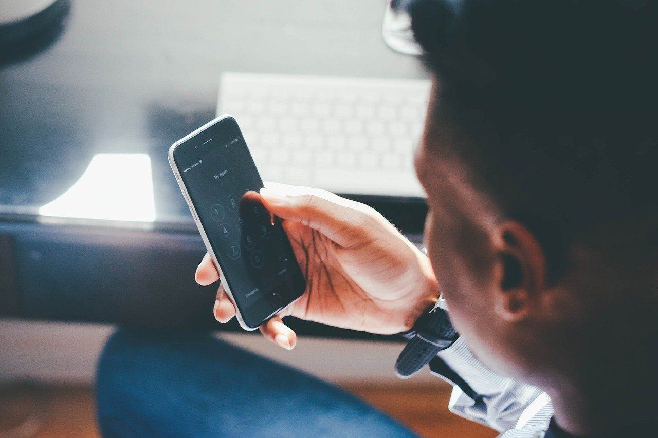 A man is holding a cell phone in his hand in front of a keyboard.