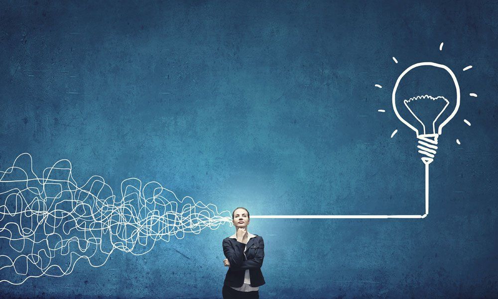 A woman is standing in front of a drawing of a light bulb.