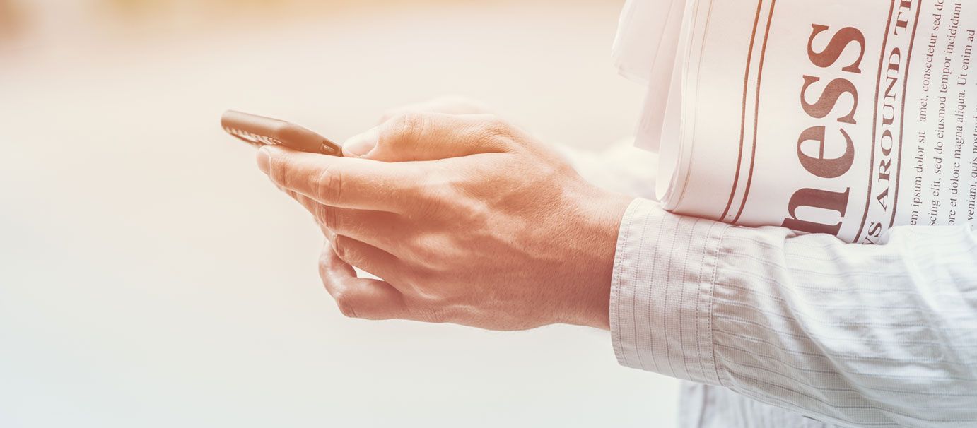 A person is holding a newspaper and using a cell phone.