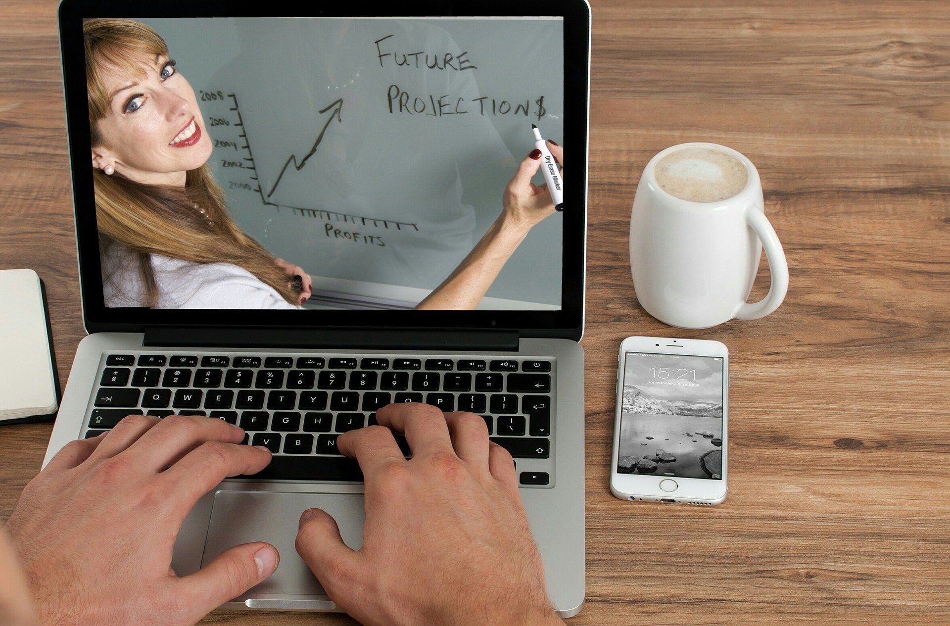 A person is typing on a laptop with a woman on the screen.