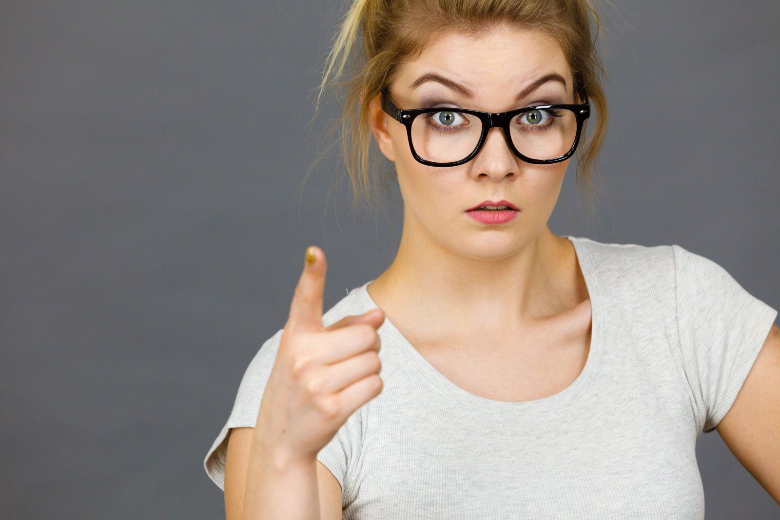 A woman wearing glasses is pointing at the camera.