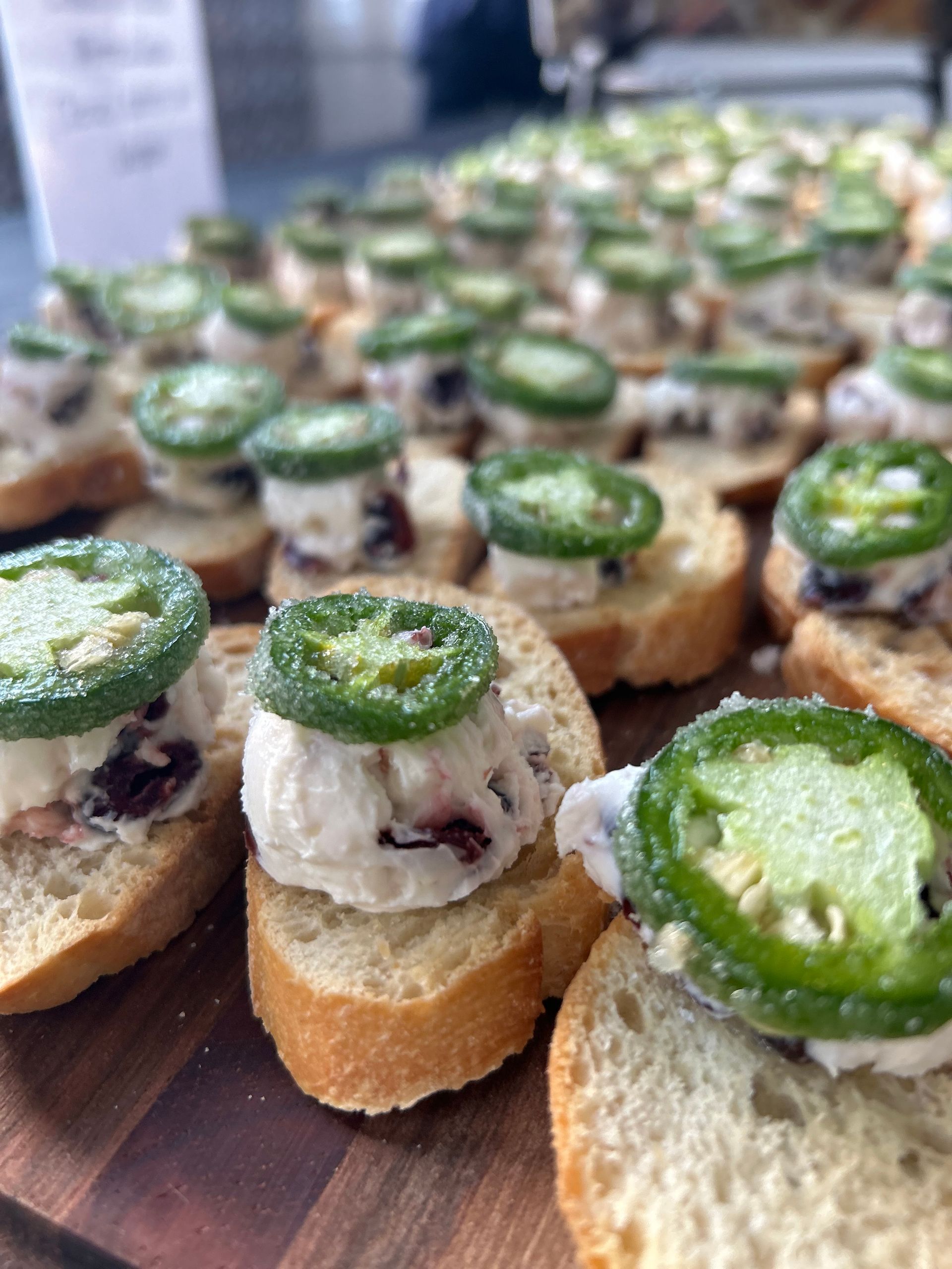 A bunch of sandwiches with jalapenos on top of them on a wooden cutting board.