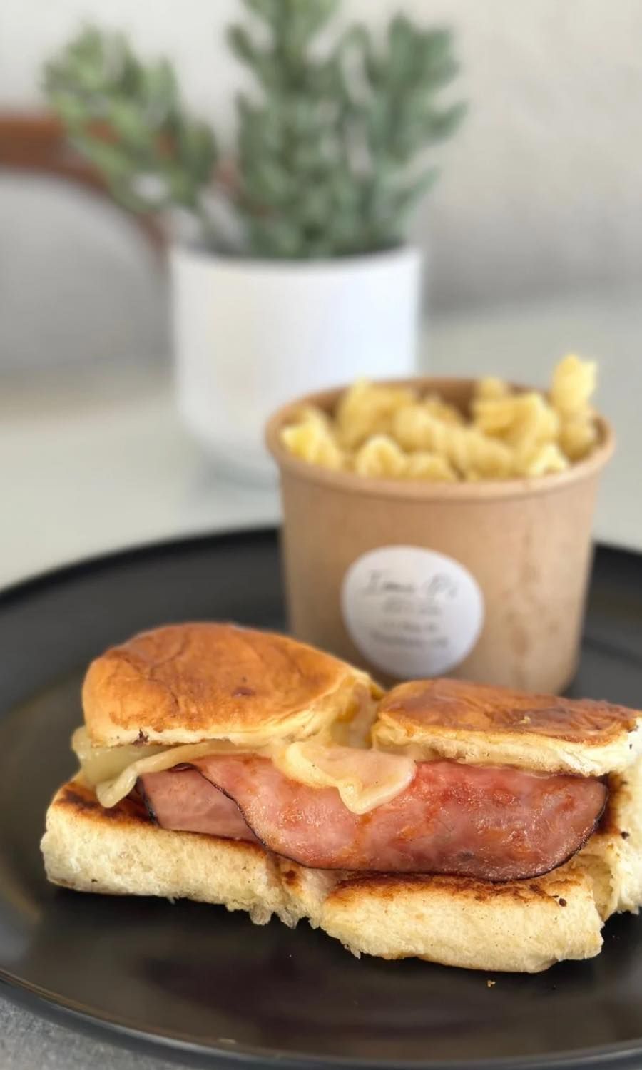 A close up of a sandwich on a plate next to a bowl of macaroni and cheese.