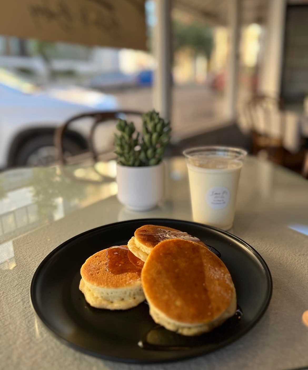 Two pancakes are on a black plate on a table next to a cup of milk.