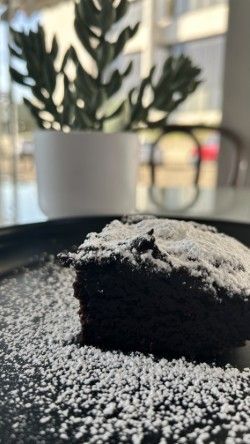 A piece of chocolate cake covered in powdered sugar on a plate.