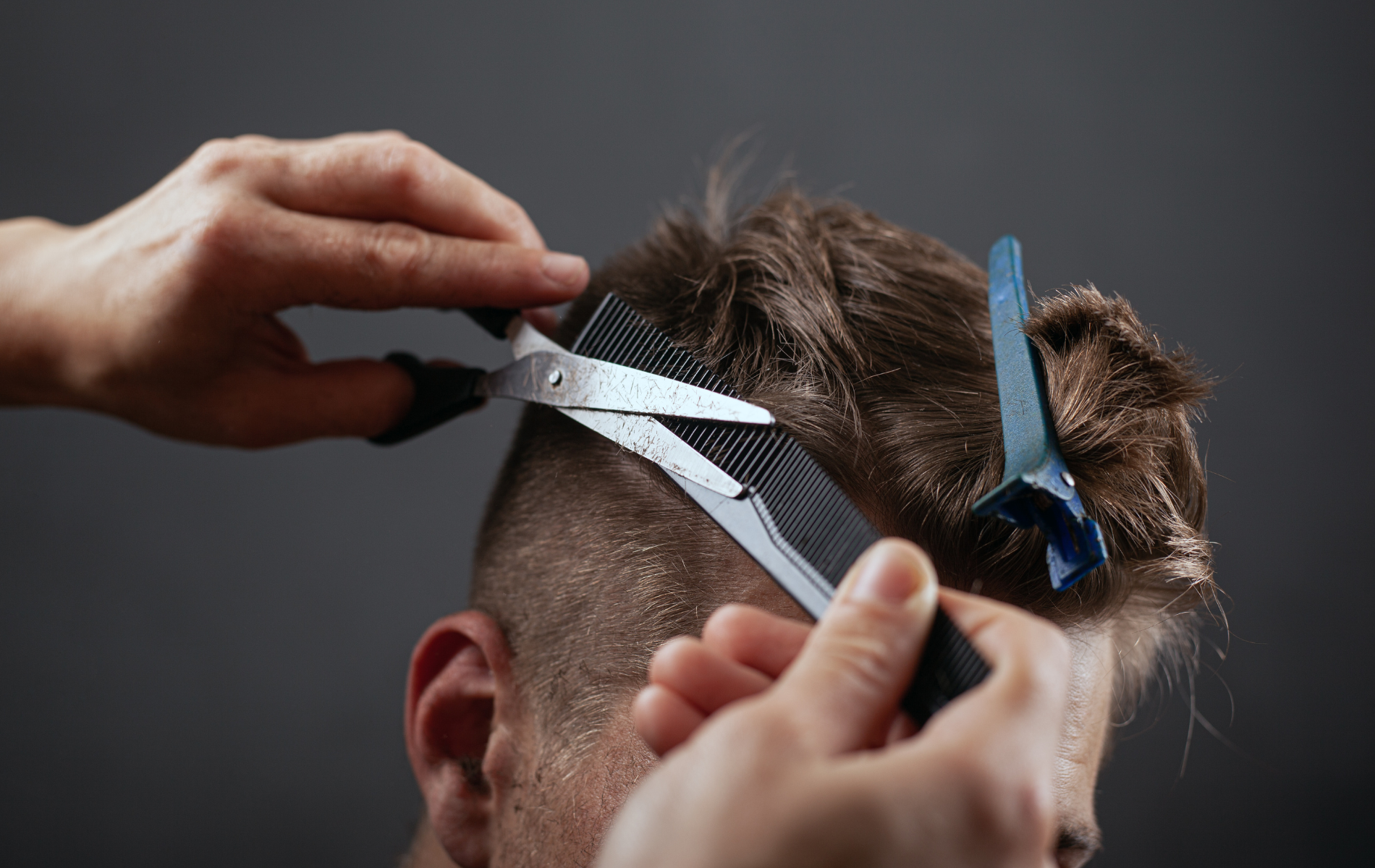 Hands cutting hair with scissors and comb. Dark background.