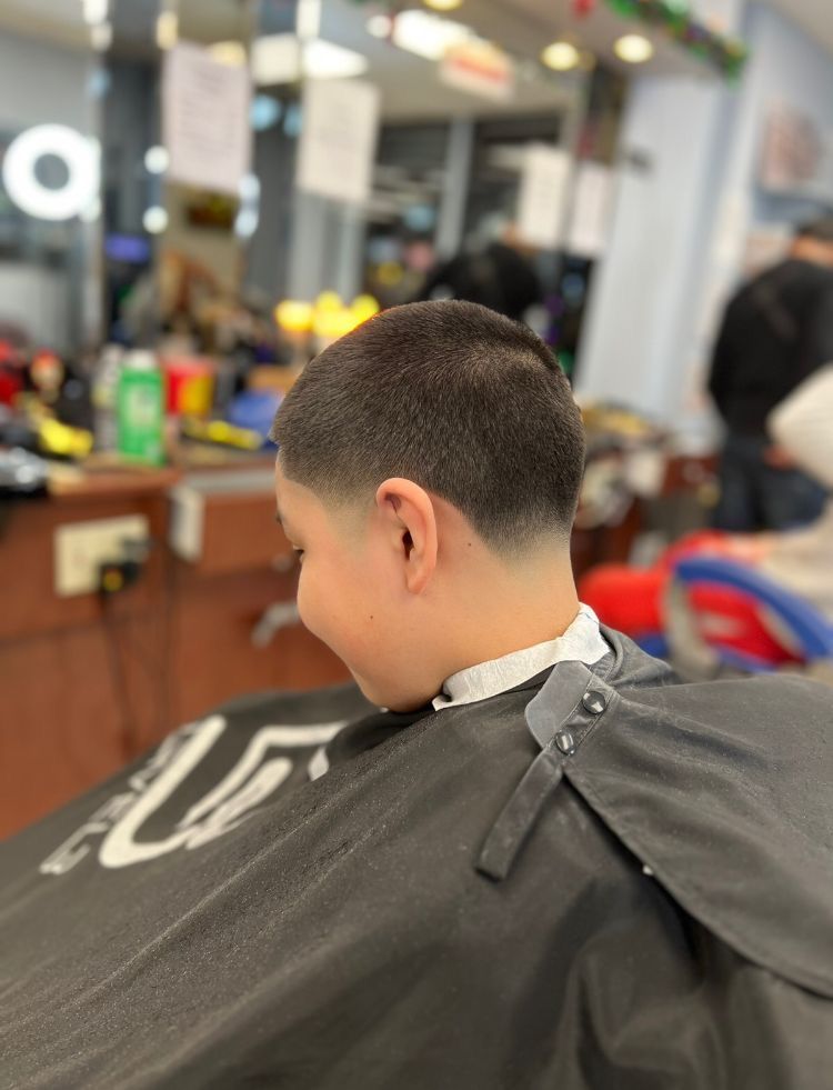 Boy with a short haircut in a barber shop, wearing a cape.