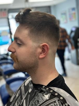 Man with a fade haircut and mustache at a barber shop, side profile view.