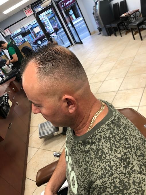 Man getting a haircut at a barbershop. He has a faded buzzcut and is wearing a camo shirt.