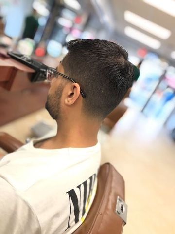 Man in a barber chair with a faded haircut, wearing a white t-shirt and glasses.