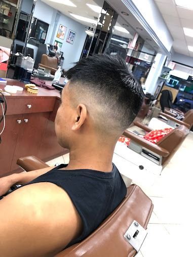 Man getting a fade haircut at a barbershop. Dark hair on top, skin fades to pale. He's sitting in a brown chair.