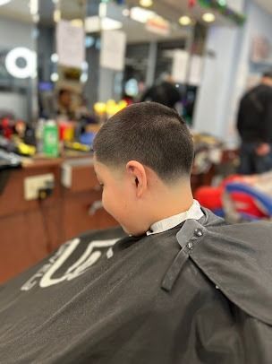 Boy in barber's chair with a faded haircut, wearing a barber cape.