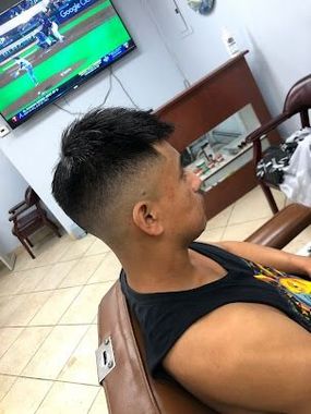 Man in a barbershop, getting a fade haircut. The man is wearing a tank top and sitting in a barber chair.