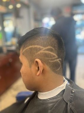 Man with a fade haircut and intricate design shaved on the side of his head in a barber shop.
