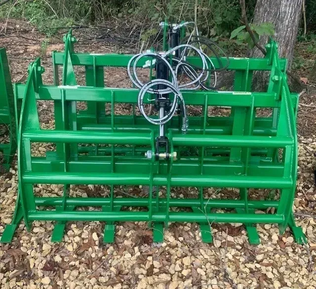 A green tractor grapple is sitting on a pile of leaves.