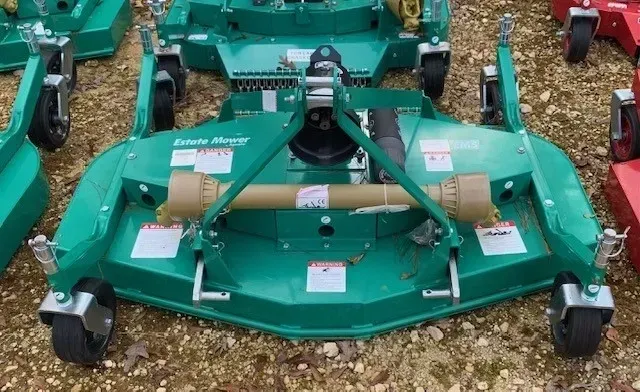A row of green lawn mowers are sitting on gravel