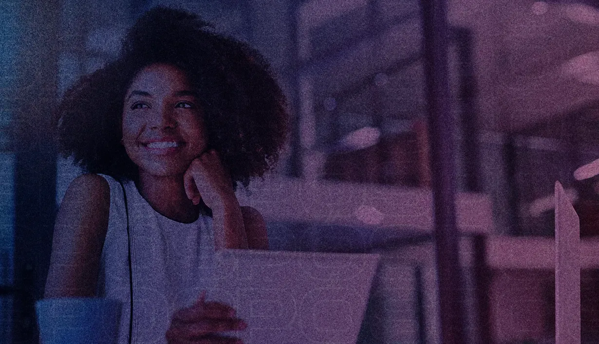 Uma mulher está sentada à mesa com um laptop e sorrindo.