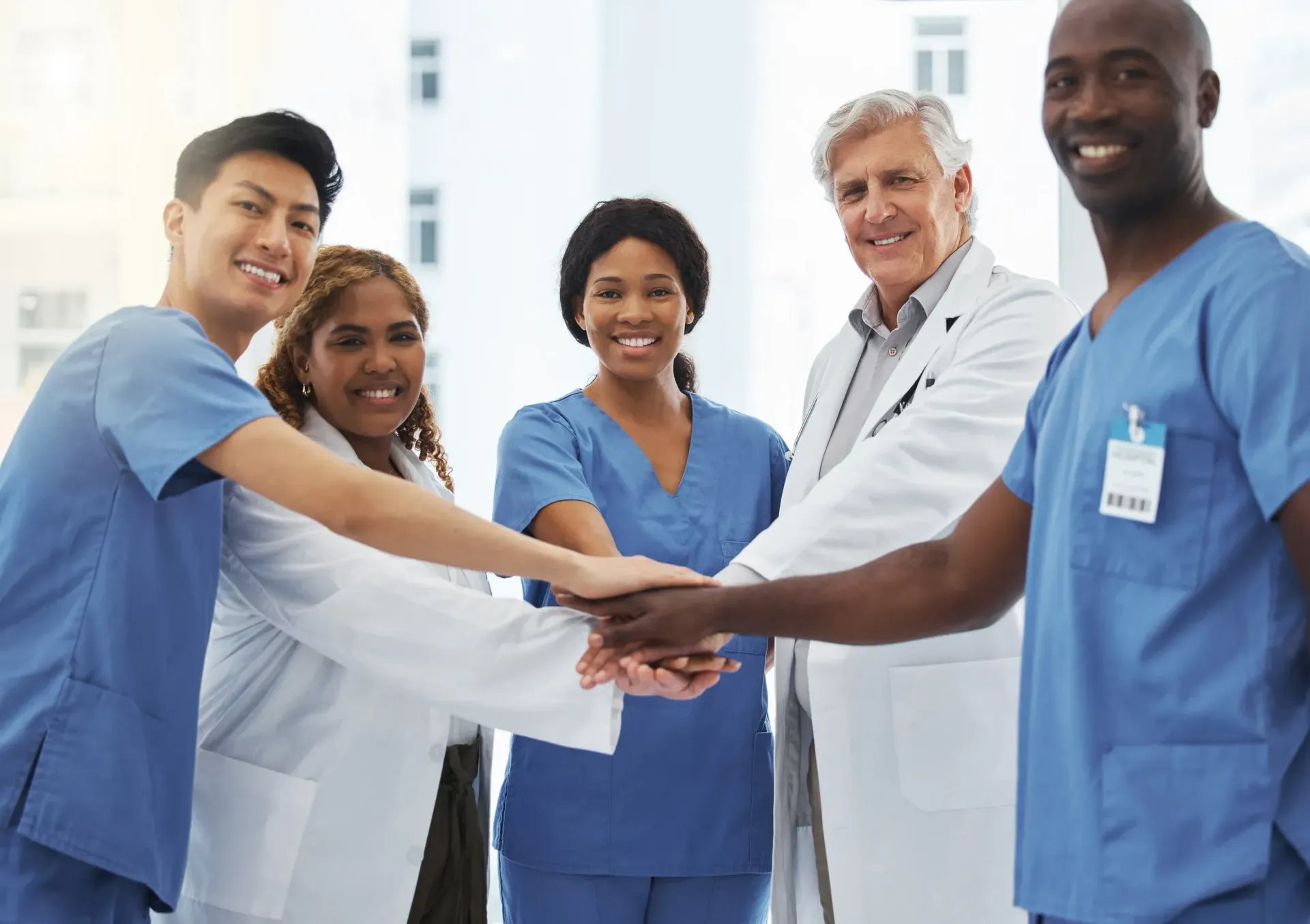 Five smiling healthcare workers in scrubs, posing against white backdrop. Five smiling healthcare workers in scrubs, posing against white backdrop.
