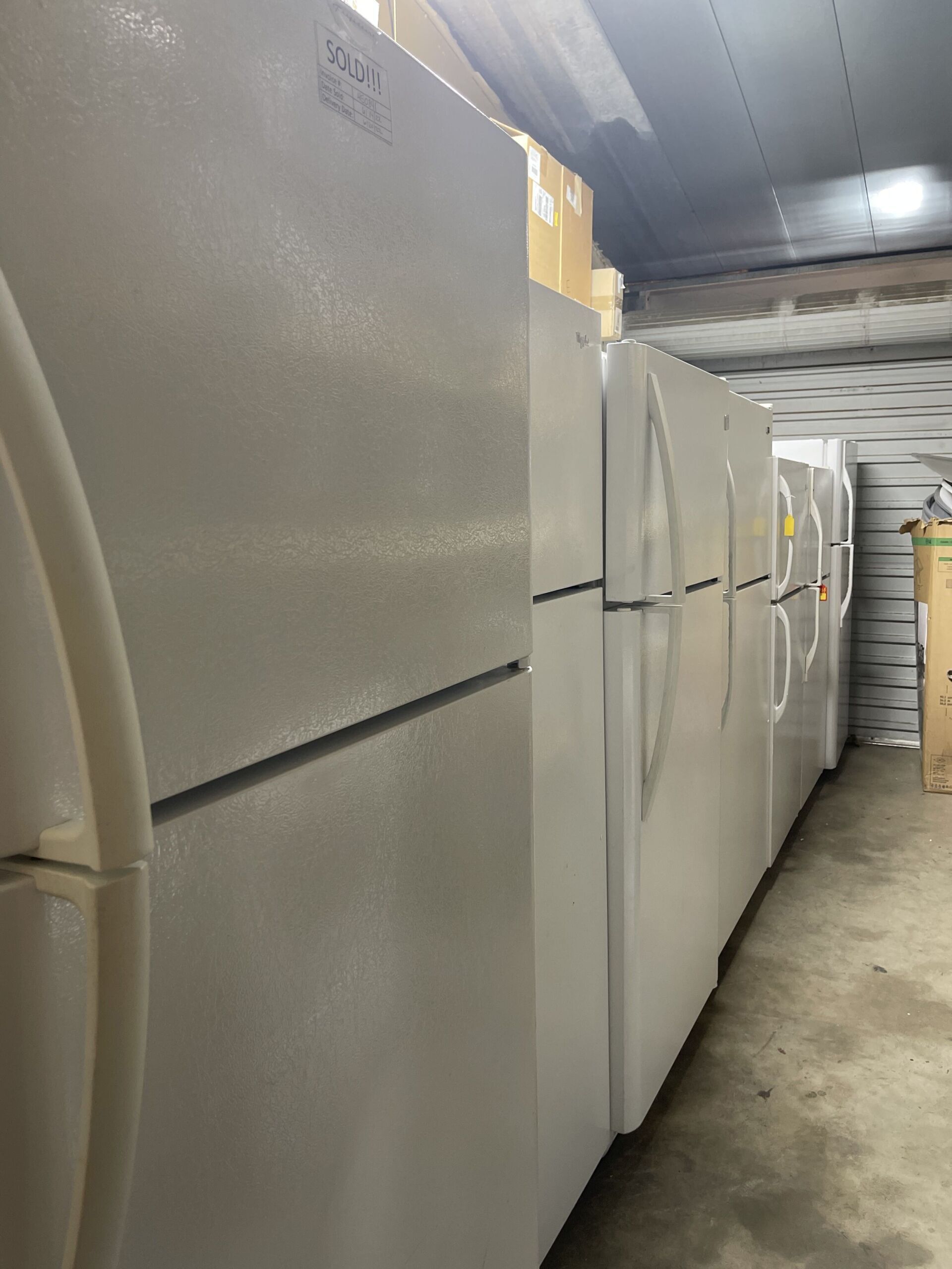 A row of white refrigerators are lined up in a garage.